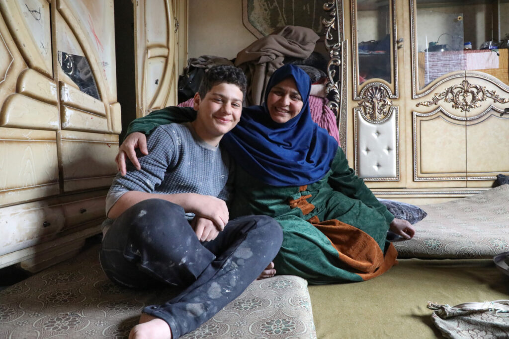 Syrian refugee returnee Ibtihal, 52, a mother of five, and her youngest son, Omar, 14, sit in their damaged house